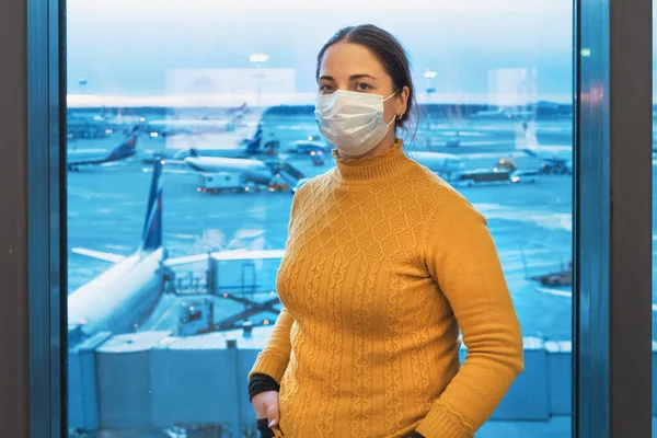 飛行を待っている飛行機の背景にある空港ターミナルのウイルス対策マスクの若い女性。コロナウイルス感染｜Covid-2019 — ストック写真