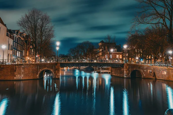 Amsterdamský průplav v noci s osvětleným mostem. Amsterdam - hlavní město cestovního ruchu Nizozemska — Stock fotografie