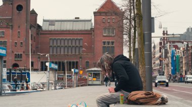 Amsterdam, Hollanda - Mart 2020: Avrupalı evsiz adam Amsterdam Caddesi, Hollanda 'da beton bankta oturuyor