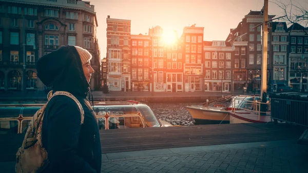 かわいい若い女性は、オランダの日没の太陽の光でアムステルダムの水上運河を歩いています。ヨーロッパ旅行の概念 — ストック写真