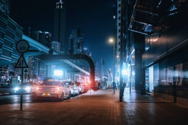 Şehir merkezindeki Dubai 'de gece caddesinde taksi arabaları, yüksek binalar ve gece aydınlatmaları var.