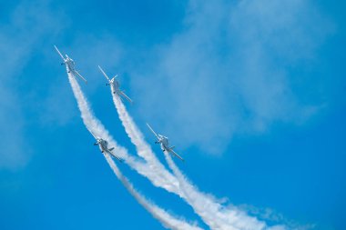 Hava gösterisinde beyaz dumanlı uçaklar görülüyor. Pilotlar mavi gökyüzü arka planında jetler üzerinde numaralar yaparlar.