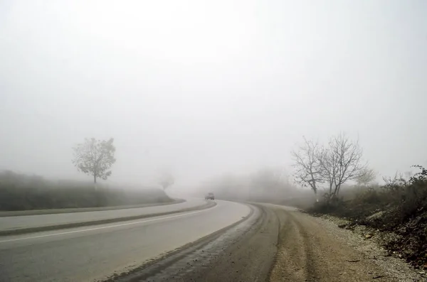 Paisagem de estrada de asfalto nebulosa entre árvores escuras nuas, ou nevoeiro na estrada para montanhas no tempo de inverno, smailli Azerbaijão — Fotografia de Stock