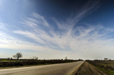 Asfalt yol ile çıplak kış alanları arasında mesafe içine basık kırsal manzara mavi gökyüzü ve yumuşak ihale bulutlar temizleyin