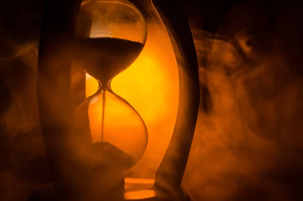 Concepto de tiempo. Silueta de reloj de arena y humo sobre fondo oscuro con luz de fondo fría de color rojo anaranjado amarillo caliente, o símbolos del tiempo con espacio de copia, vidrio de arena o reloj de arena —  Fotos de Stock