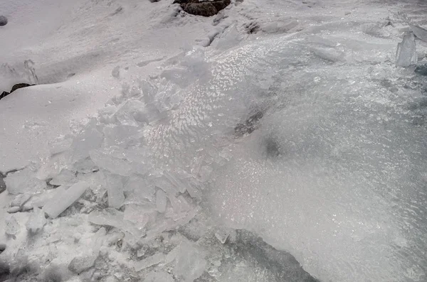 Vista esterna di blocchi di ghiaccio in acqua ghiacciata in struttura invernale con neve bianca leggera che copre pezzi di ghiaccio incrinato su un terreno invernale ghiacciato — Foto Stock