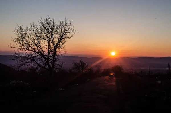 Paesaggio autunnale o invernale con strada e alberi. La luce dorata irradia il tramonto. Su uno sfondo di montagne e il cielo con le nuvole. Azerbaigian Caucaso — Foto Stock