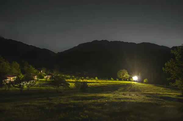 Paisaje nocturno panorama de montaña. valle con hierba en la ladera de la cordillera. Pradera verde con casas y luz fuerte. Cáucaso, Lahic, Azerbaiyán — Foto de Stock