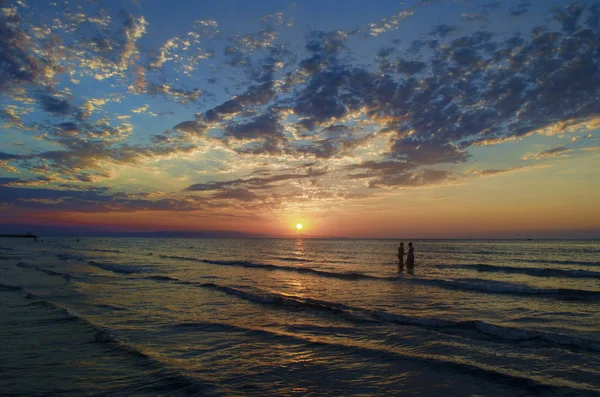 Giovani ragazze in acqua calda al tramonto. Splendidi colori nel cielo e nel mare. Persone in piedi e guardando il tramonto sul Mar Caspio. Baku, Azerbaigian. Forme perfette riflesse nell'acqua — Foto Stock