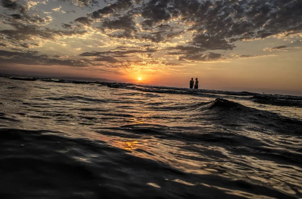 Raparigas em água morna ao pôr do sol. Cores lindas no céu e no mar. Pessoas de pé e assistindo ao pôr do sol no mar Cáspio. Baku, Azerbaijão. Formas perfeitas refletidas na água — Fotografia de Stock