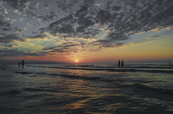 Jonge meisjes in warm water bij zonsondergang. Prachtige kleuren in de lucht en de zee. Mensen staan en kijken naar de zonsondergang op de Kaspische Zee. Baku, Azerbeidzjan. Perfecte vormen weerspiegeld in water — Stockfoto