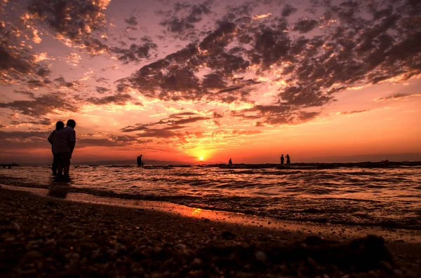 Młode dziewczyny w ciepłej wodzie o zachodzie słońca. Wspaniałe kolory nieba i morza. Ludzie stojący i oglądać zachód słońca na Morzu Kaspijskim. Baku, Azerbejdżan. Idealne kształty odbicie w wodzie — Zdjęcie stockowe