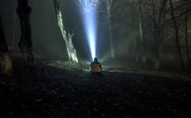 yerde oturan adam ile gece, mistik manzara gerçeküstü ışıkları karanlık bir ürkütücü ormandaki garip siluet