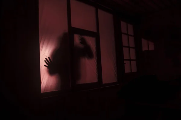 Horror concept. Het silhouet van een mens met gespoten armen voor een raam. 's nachts. — Stockfoto