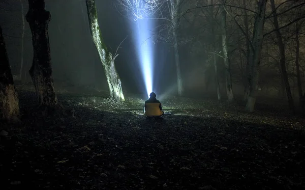 在夜间的黑暗的幽灵森林的奇怪剪影，神秘景观超现实灯与坐在地面上的人 — 图库照片