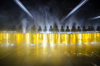 Vape kavramı. Duman bulutları ve vape sıvı şişe koyu arka plan üzerinde. Işık efektleri.