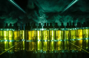 Vape kavramı. Duman bulutları ve vape sıvı şişe koyu arka plan üzerinde. Işık efektleri.