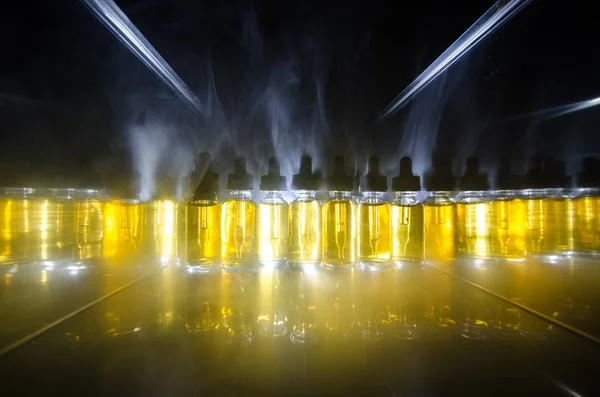 Concepto Vape. Nubes de humo y botellas de vapor líquido sobre fondo oscuro. Efectos luminosos . — Foto de Stock