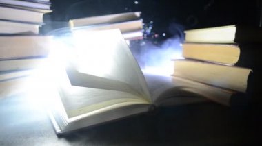 Bir yığın halinde birçok eski kitaplar. Knoledge kavramı. Duman elemanları ile karanlık bir arka plan üzerinde kitaplar. Merkezi büyülenmiş kitapta. Glasswatch