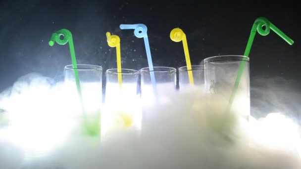 П'ять коктейлів на барі з димом на темному тлі. Жовті, зелені та сині окуляри. Клубні напої — стокове відео