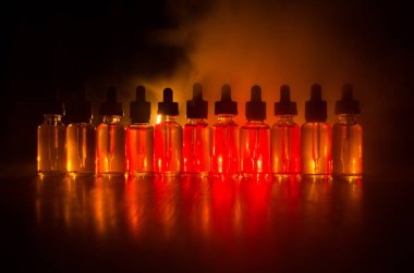 Vape kavramı. Duman bulutları ve vape sıvı şişe koyu arka plan üzerinde. Işık efektleri.