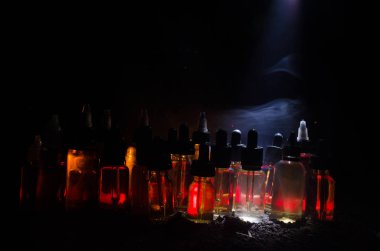 Vape kavramı. Duman bulutları ve vape sıvı şişe koyu arka plan üzerinde. Işık efektleri.