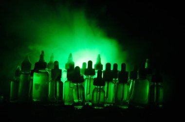 Vape kavramı. Duman bulutları ve vape sıvı şişe koyu arka plan üzerinde. Işık efektleri.
