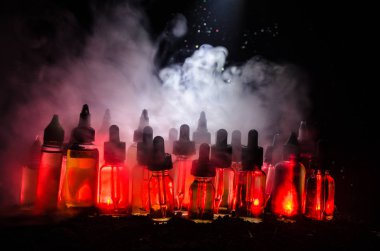 Vape kavramı. Duman bulutları ve vape sıvı şişe koyu arka plan üzerinde. Işık efektleri.