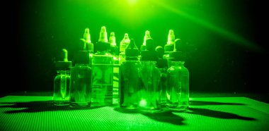 Vape kavramı. Duman bulutları ve vape sıvı şişe koyu arka plan üzerinde. Işık efektleri.