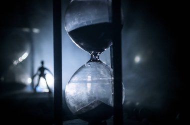 Zaman kavramı. Duman ile hourglasses ve karanlık bir arka plan ışıkları arasında duran bir adam silüeti.