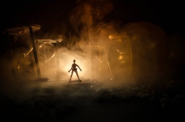 Zaman kavramı. Duman ile hourglasses ve karanlık bir arka plan ışıkları arasında duran bir adam silüeti.