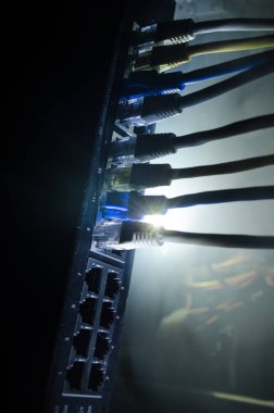 Ağ anahtarı ve ethernet kabloları, global iletişim sembolüdür. Işıklar ve duman ile koyu arka plan üzerinde renkli ağ kabloları. Seçici odak