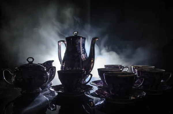 Comida fondo té y café tema. Tetera de cerámica antigua o cafetera con jarra de tazas y taza de azúcar sobre fondo oscuro con luces y humo. Siluetas de tetera y taza de cerámica . — Foto de Stock
