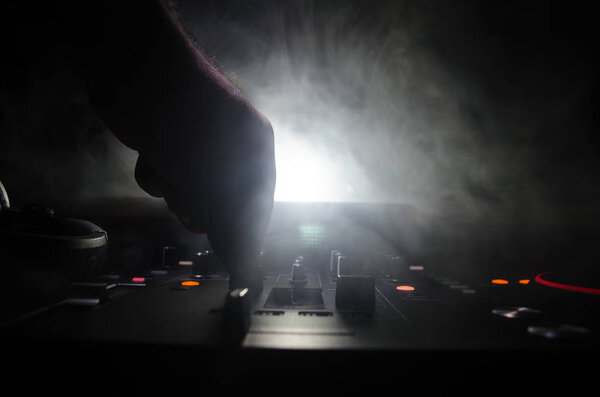 DJ Spinning, Mixing, and Scratching in a Night Club, Hands of dj tweak various track controls on dj's deck, strobe lights and fog, selective focus, close up. Dj Music club life concept