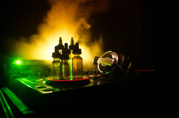 Concepto de Vape y DJ Club. Nubes de humo y botellas de vapor líquido en Dj mezclador de cerca. Efectos de luz. Útil como fondo o publicidad de vapor o club o fondo de vapor . — Foto de Stock
