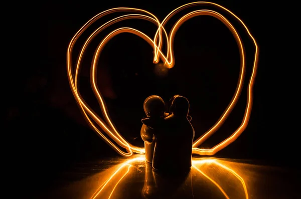 Two young lovers paint a heart on fire. Silhouette of couple and Love words on a dark background — Stock Photo, Image