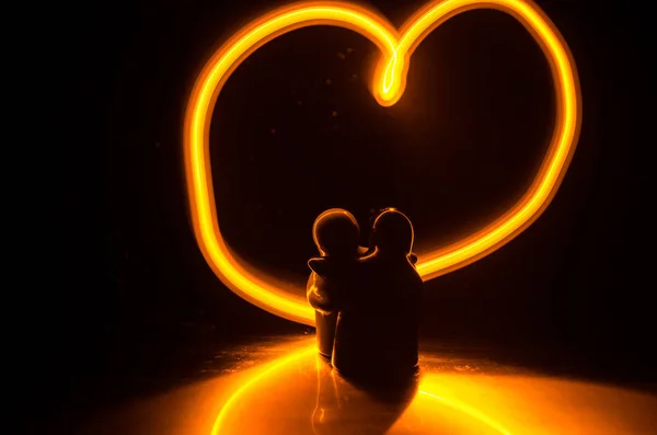 Dois jovens amantes pintam um coração em chamas. Silhueta de casal e palavras de amor em um fundo escuro — Fotografia de Stock