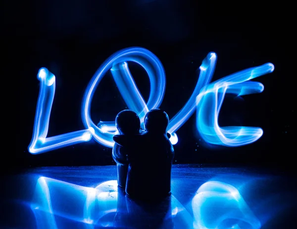 Two young lovers paint a heart on fire. Silhouette of couple and Love words on a dark background — Stock Photo, Image