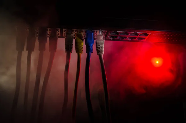 Сетевой коммутатор и Ethernet кабели, символ глобальных коммуникаций. Цветные сетевые кабели на тёмном фоне с огнями и дымом. Селективный фокус — стоковое фото