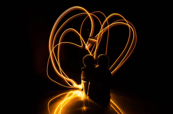 Two young lovers paint a heart on fire. Silhouette of couple and Love words on a dark background — Stock Photo, Image