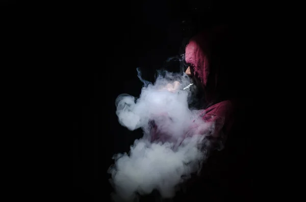 Hombre aspirante sosteniendo un mod. Una nube de vapor. Fondo negro. Vapeando un cigarrillo electrónico con mucho humo — Foto de Stock