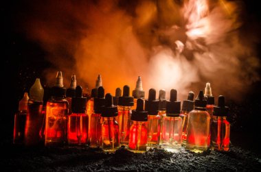 Vape kavramı. Duman bulutları ve vape sıvı şişe koyu arka plan üzerinde. Işık efektleri.