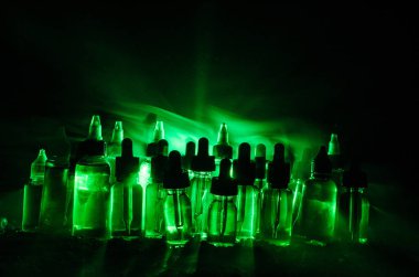 Vape kavramı. Duman bulutları ve vape sıvı şişe koyu arka plan üzerinde. Işık efektleri.