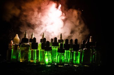 Vape kavramı. Duman bulutları ve vape sıvı şişe koyu arka plan üzerinde. Işık efektleri.