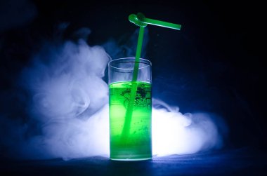 Yeşil duman ve backlights ile koyu arka plan üzerinde saman ile kokteyl bardak.