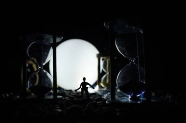 Zaman kavramı. Duman ile hourglasses ve karanlık bir arka plan ışıkları arasında duran bir adam silüeti.