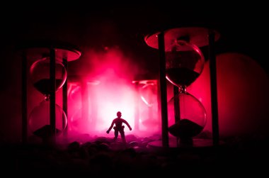 Zaman kavramı. Duman ile hourglasses ve karanlık bir arka plan ışıkları arasında duran bir adam silüeti.