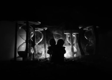 Zaman ve aşk kavramı. Oyuncak seramik figürleri hourglasses sis ile karanlık yanan arka plan arasında sarılma siluetleri