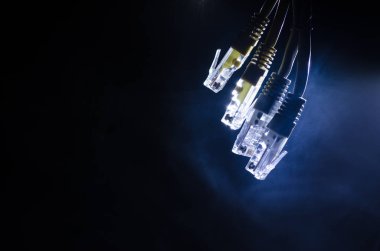 Ağ anahtarı ve ethernet kabloları, global iletişim sembolüdür. Işıklar ve duman ile koyu arka plan üzerinde renkli ağ kabloları. Seçici odak