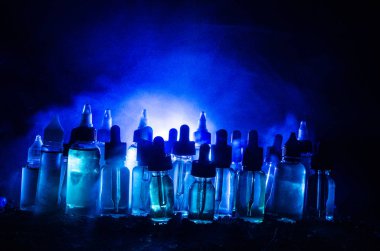 Vape kavramı. Duman bulutları ve vape sıvı şişe koyu arka plan üzerinde. Işık efektleri.